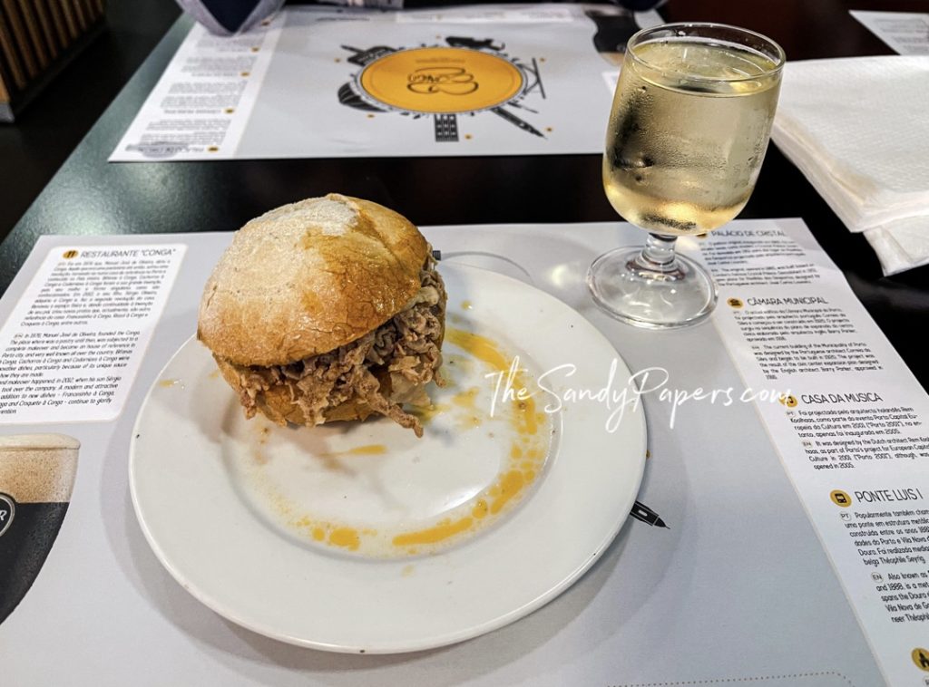 A sandwich with pulled meat and a glass of white wine.
